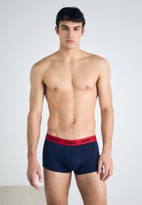 Námornícke modré boxerky s červeným elastickým pásom, na ktorom je čierny nápis značky "HUGO". Mäkký, textúrovaný materiál, priliehavý strih.