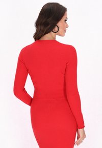 Roter, gerippter Pullover mit langen Ärmeln und taillierter Passform. Mit rundem Ausschnitt und dekorativen Besätzen an den Ärmelbündchen. Glatte Textur.