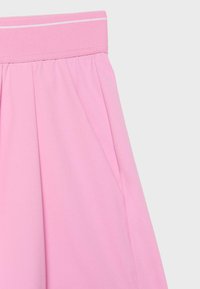 Jupe rose taille haute avec une large ceinture et des plis subtils, montrant une poche de couture latérale sur un fond uni.