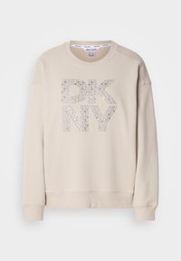 Sweat-shirt beige à manches longues et col rond avec lettres "DKNY" décorées de sequins argentés sur le devant.