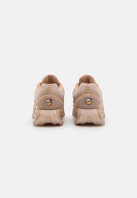Beige sneakers with mesh upper, padded collar, and textured rubber sole. Features logo patch on heel and cushioned insole.