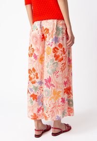 Floral maxi skirt in pink with orange, purple, and green patterns. Lightweight fabric with a flowy design. Paired with red sandals.