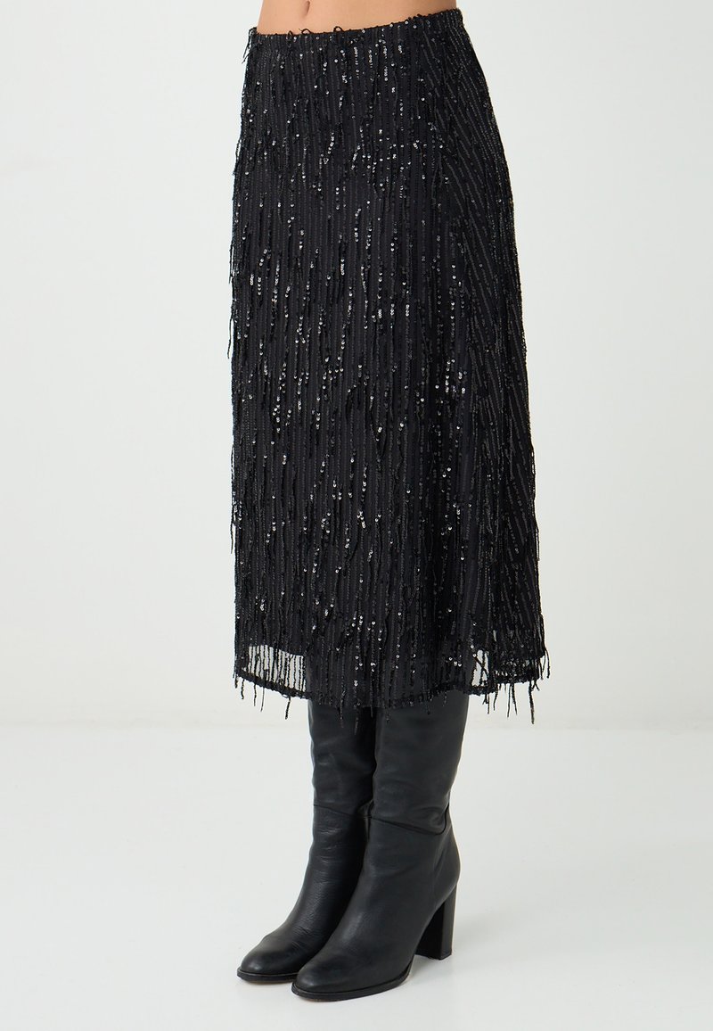Gonna nera con frange caratterizzata da una finitura testurizzata e paillettes sparse. Abbinata a stivali neri alti fino al ginocchio e con orlo dritto.