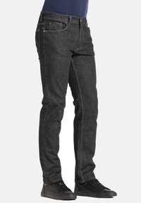 Donkergrijze denim jeans met een slanke pasvorm, voorzien van vijf zakken, riemlussen en contrasterende stiksels. Gecombineerd met zwarte sneakers.