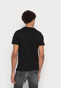 Svart kortärmad t-shirt i slät tyg, med rund halsringning och minimalistisk design, bärs tillsammans med mörkgrå jeans.