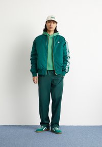 Vihreä pommikapteenitakki valkoisilla raidoilla, vihreä huppari, yhteensopivat urheiluhousut ja vihreät lenkkarit valkoisilla yksityiskohdilla. Vaalean värinen lippalakki.