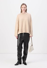 Beige strikkegenser med løs passform og ribbestrikket kant, parret med svarte skinnbukser og spisse svarte ankelboots. Inkluderer en hvit håndveske.