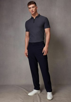 Pantalones cargo azul marino con bolsillos laterales, combinados con un polo gris oscuro texturizado con cierre de cremallera. Zapatillas blancas completan el atuendo.