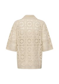 Haut en crochet beige avec manches courtes larges et motifs floraux circulaires, vu de dos.