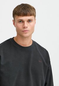 Musta puuvillast lahtine särk, millel on sooniline krae, minimalistlik disain ja väikese burgundia toonis logoga vasakul rinnal.