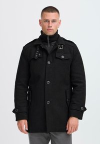 Schwarzer Wollmantel mit hohem Kragen, geknöpftem Vorderteil und mehreren Taschen. Verfügt über eine zusätzliche gefütterte Innenlage und dekorative Beschläge.
