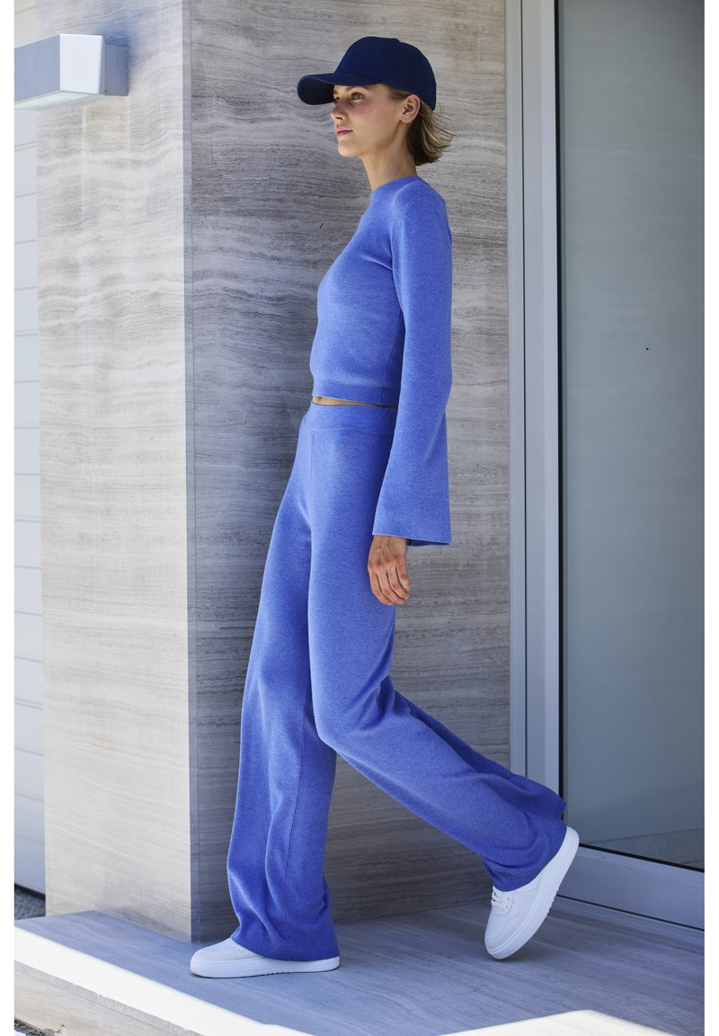 Plavi pleteni pulover dugih rukava i odgovarajuće široke hlače, s nešto skraćenim dizajnom. Uparen s bijelim tenisicama i mornarskom kapom.