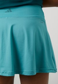 Una gonnellina sportiva turchese chiaro realizzata in materiale traspirante, caratterizzata da un motivo testurizzato, vita elastica e un discreto logo del marchio.