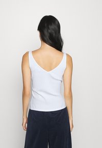 Ljusblå ribbad ärmklänning med V-ringning, ärmlös modell och en figurnära silhuett, tillsammans med mörka strukturerade byxor.