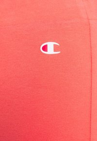 Červená tkanina s bílým a červeným logem značky Champion umístěným ve středu poblíž švů na pravé straně.