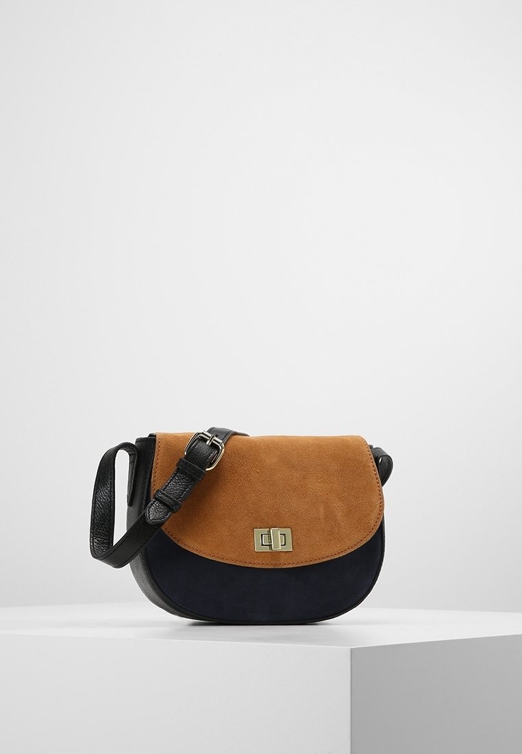 Bolso de solapa de ante marrón con cuerpo azul marino y correa de cuero negra. Presenta un cierre dorado y un diseño redondeado, adecuado para uso casual.