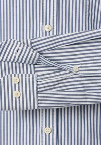 Blauw-wit gestreepte blouse met lange mouwen, met knoopmanchetten en knopen aan de voorkant, die een close-up toont van de stof en stiksels.