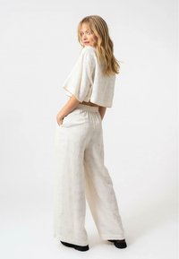 Top corto bianco con maniche larghe e pantaloni palazzo a vita alta, morbidi. Tessuto testurizzato con dettagli di trama sottili. Calzature nere.