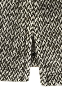 Gestrickter Stoff mit Hahnentrittmuster in Schwarz und Weiß, mit strukturierter Oberfläche und einem Ausschnittdetail am unteren Rand.