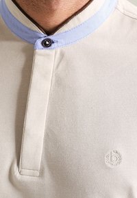 Close-up of a light-colored polo shirt featuring a contrasting light blue collar and a small embroidered logo on the chest.