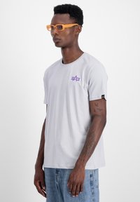 Hall grey t-särk pehmest kangast, millel on vasakul rinnal lilla logo. Mudel kannab oranže ristkülikukujulisi prille. Mugav lõige.