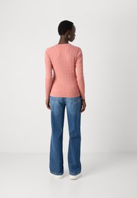 Pulover roz din tricotaj cu model de lână, cu mâneci lungi, design ajustat, tiv și manșete cu nervuri, purtat cu blugi lejeri albaștri și adidași albi.