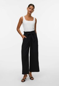 Zwarte wijde broek met een strik taille, gecombineerd met een aansluitend wit hemdtopje. De stof lijkt lichtgewicht met een gladde textuur.