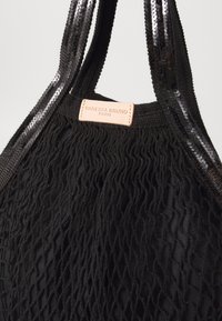 Borsa a rete nera con un design testurizzato, dotata di manici lucidi neri con paillettes e di un'etichetta in pelle marrone chiaro impresso con "Vanessa Bruno Paris."