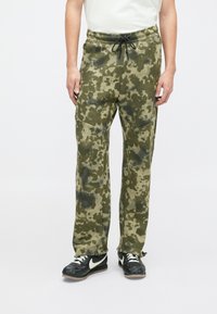 Olive zaļas krāsas kamuflāžas jogger bikses ar brīvu piegriezumu, teksturēta auduma, elastīga jostasvieta un sānu kabatas. Melna aukliņa regulēšanai.
