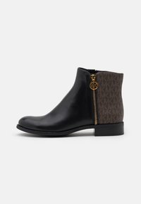 Botte de cheville en cuir noir avec un dos à motif marron, zip doré accentué du logo, bout arrondi et talon bas.
