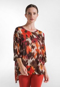 Løs pasform, multikrom top med et abstrakt mønster i orange, brun og creme. Har en rund hals og brede ærmer.