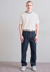 Fehér póló szürke nyakkivágással, sötét farmer egyenes szárú nadrág és fehér sportcipő. Egyszerű design, laza fazon és minimális részletezés.