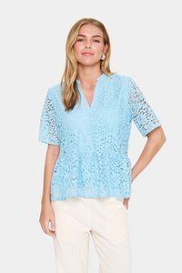 Mėlynos spalvos nėriniųblauzelė su peplumo dizainu, trumpomis rankovėmis ir V formos iškirpte. Nėriniai turi sudėtingus gėlių raštus.