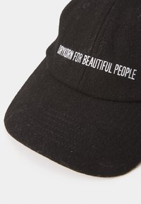 Schwarze Wollmütze mit dem Aufdruck "DRYKORN FOR BEAUTIFUL PEOPLE" in weißer Schrift auf der Vorderseite. Gebogenes Schild mit sichtbaren Nähten.