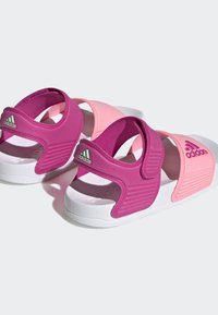 Sandále Adidas s ružovými a fialovými popruhmi, nastaviteľným suchým zipsom, bielou vystlanou podrážkou a textúrovanými detailmi na strane.