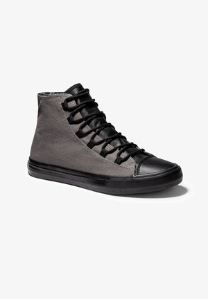 Zapatilla alta con laterales de tela gris, puntera y lengüeta de cuero negro, cordones negros y suela de goma negra sobre fondo blanco.