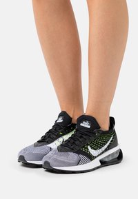 Svartvita mönstrade Nike-sneakers med gröna accenter, nätmaterial och en synlig luftdämpningsenhet. Svarta snören och logotyp på tungan.