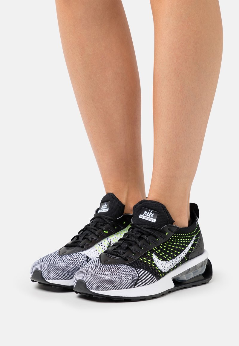 Svartvita mönstrade Nike-sneakers med gröna accenter, nätmaterial och en synlig luftdämpningsenhet. Svarta snören och logotyp på tungan.