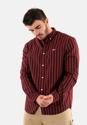 Camisa de manga larga burdeos con rayas verticales blancas, cuello abotonado y pequeño logo en el pecho. Tejido de algodón con una textura suave.
