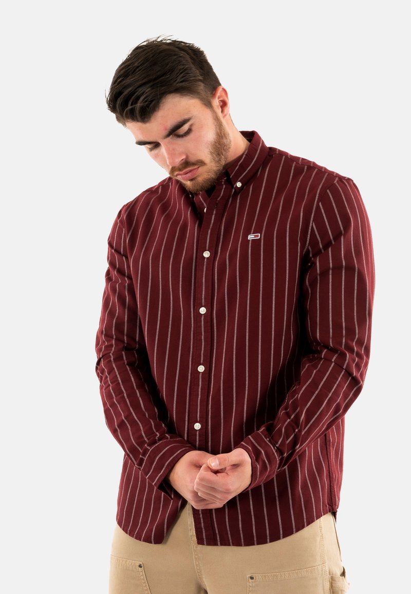 Camicia bordeaux a maniche lunghe con righe verticali bianche, colletto button-down e piccolo logo sul petto. Tessuto di cotone con una consistenza liscia.