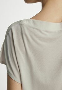 Jasnoszara bluzka wykonana z miękkiego, lekkiego materiału o luźnym kroju. Projekt obejmuje szeroki dekolt i krótkie rękawy.