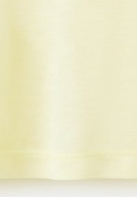 Gros plan sur un tissu jaune pâle avec des coutures visibles le long de l'ourlet sur un fond lisse et clair.