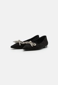 Ballerines noires en daim avec un bout pointu, ornées d'un nœud en corde argentée décoratif à l'avant et d'un petit talon noir uni.