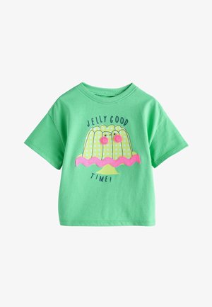 Chemise verte à manches courtes avec une illustration de dessert à la gelée à carreaux jaunes, des yeux pompons roses, un bord ondulé rose et le texte "Jelly Good Time !"