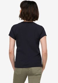 Krátký rukáv, námořnická bavlněná tričko s kulatým výstřihem a volným střihem, ukazující zadní pohled s viditelným švem a hladkou texturou.