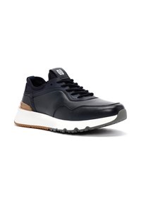 Marineblauwe leren sneaker met een gestructureerd ontwerp, zwarte veters en een witte tussenzool. Heeft een gemêleerd bruin accent op de hak en een rubberen zool.