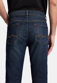 Mörkblå denimjeans med rak passform, med gula sömmar på bakfickorna och en enkel midjebandsdesign.