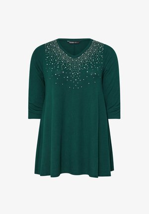 Tunica verde realizzata in tessuto morbido, con scollo a V e maniche a tre quarti. Decorata con borchie argentate sparse sul davanti.