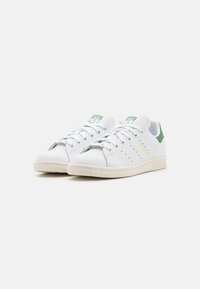 Weiße Adidas Stan Smith Sneakers mit grüner Ferse und perforierten Streifen, nebeneinander auf einem schlichten weißen Hintergrund platziert.