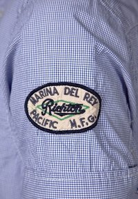 Tessuto a quadretti blu e bianchi con una toppa ricamata. La toppa presenta "Marina del Rey", "Richton" e "Pacific M.F.G." in ricamo.